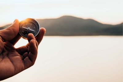 Hand with compass at mountain road at sunset sky