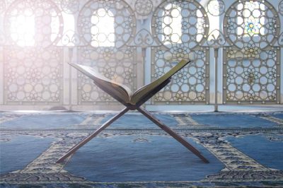 Open Quran on a wooden stand placed on a mosque carpet with decorative background panels